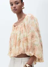 Blusa de gasa color crema con estampado de flores en tonos naranja y verde, escote cuadrado con detalle fruncido, mangas largas abullonadas y espalda abierta.