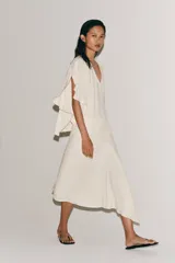 Falda midi de tiro medio, color blanco off-white, confeccionada en hilatura de viscosa. Presenta un diseño fluido, con bajo asimétrico y detalle de caída drapeada en el lateral. Cierre con cremallera oculta en costura.