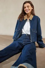 Sobrecamisa de denim azul oscuro, con cuello de pana color camel, cierre frontal de cremallera y dos bolsillos frontales con tapa y botón.