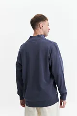 Buzo de tejido de punto color verde oliva, con cuello alto y cierre frontal parcial. Presenta un pequeño logo bordado en el pecho.