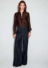 Camisa de satén color marrón chocolate, con cuello camisero, cierre frontal de botones ocultos y mangas largas con puños abotonados. Presenta un diseño recto adornado con pequeños detalles de strass brillantes distribuidos por toda la prenda.