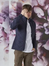 Campera azul marino con cierre frontal, cuello alto y bolsillos laterales con cierre. Tiene un parche rojo con cierre en la manga izquierda y un diseño acolchado en la parte delantera.