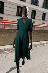 Vestido midi de color marrón chocolate, con escote en pico y mangas cortas abullonadas con puños elásticos. Presenta costuras verticales decorativas en el frente y cierre de cremallera oculta en la espalda.