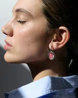 Aros tipo argolla de plata con dije circular de resina con diseño estampado de flores pequeñas en color bordó sobre fondo blanco.