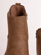 Bota tipo chelsea de cuero sintético color marrón, con paneles laterales elásticos y suela de goma blanca con relieve dentado.