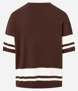 Remera oversized deportiva color marrón con cuello en V, rayas blancas en las mangas y en la parte inferior, y el número "62" estampado en blanco en el frente. Incluye el bordado "Humanity" y un logo de globo terráqueo.