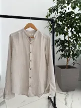 Camisa de lino a rayas beige y blancas, con cuello mao y cierre frontal de botones marrones, de manga larga.