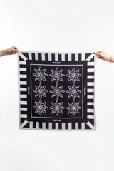 Pañuelo cuadrado negro con estampado de flores blancas y borde con diseño geométrico a rayas blancas y negras.