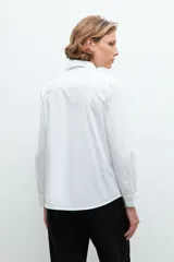 Camisa blanca de manga larga con cuello clásico y cierre frontal con botones. Presenta dos bolsillos plaqué en el pecho.