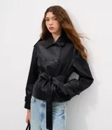 Campera tipo trench de cuero sintético (PU) color negro, con cuello solapa, cierre frontal de doble botonadura y lazo ajustable en la cintura. Presenta detalles utilitarios en los hombros y puños, con un diseño estructurado y moderno.