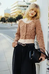 Cropped top de manga larga color marrón en punto estilo crochet con diseño en hilo de chenilla y ribetes festoneados. Cuenta con escote en U y botones forrados al frente, con forro de punto.