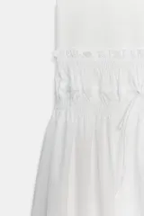 Vestido midi de color blanco con cuello redondo y manga sisa, confeccionado con un diseño combinado que presenta un cuerpo de tejido liso y una falda vaporosa con cintura elástica fruncida y cordón ajustable.