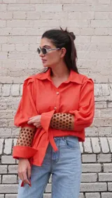Camisa de lino color naranja, con mangas largas abuchonadas, cuello camisero y cierre frontal con botones. Presenta un diseño único con detalle calado en los puños.