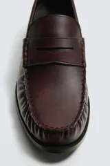 Mocasín de vestir tipo penny loafer en color bordó con acabado desgastado, diseño de antifaz en el empeine y suela de goma a contraste con pequeño tacón.