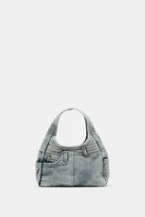 Bolso de mano tipo hobo confeccionado en tejido denim con diseño inspirado en un jean, incluyendo detalles de bolsillos exteriores, costuras reforzadas y trabillas. Cuenta con cierre de botón imantado y asa integrada.
