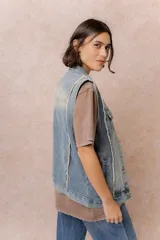 Chaleco de jean con diseño oversized y lavado vintage. Presenta cuello camisero, cierre frontal con botones metálicos, bolsillos superiores con tapa y botón, bolsillos laterales y terminaciones desflecadas en las sisas.