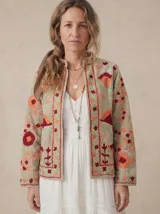 Chaqueta de terciopelo color beige con bordados florales en tonos naranja, rojo y verde. Presenta cuello mao y diseño abierto en el frente.