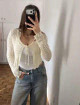 Cardigan de punto calado color marfil, con mangas largas y cierre frontal mediante lazos.
