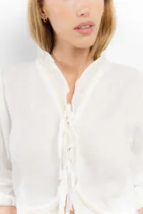 Blusa corta blanca de lino con mangas 3/4 abullonadas, escote en V con volados y cierre con lazos.