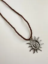 Collar con dije de sol en acero quirúrgico y cordón tipo tiento color blanco.
