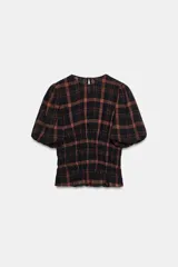 Camisa de cuello redondo y manga corta abullonada, con diseño de cuadros en tonos negro y marrón. Presenta un cuerpo entallado mediante frunces elásticos en la cintura y cierre posterior con abertura y botón.