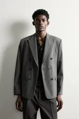Blazer de corte relaxed fit color gris, confeccionado en tejido con lana. Cuenta con solapas de pico, manga larga con botones en los puños, bolsillos con solapa en la cadera y un bolsillo de vivo en el pecho. Presenta cierre frontal de botonadura cruzada con botones oscuros.