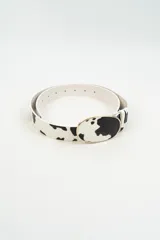 Cinturón con estampado de vaca en blanco y negro, con hebilla ovalada metálica dorada.