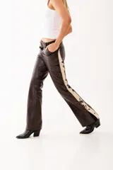 Pantalón de cuero genuino color chocolate, con paneles laterales en cuero beige. Presenta ajuste con cordones en la cintura y en los laterales de las piernas, permitiendo regular el entalle.