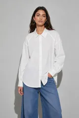 Camisa blanca de manga larga, corte holgado y diseño clásico con cuello camisero y cierre frontal de botones.