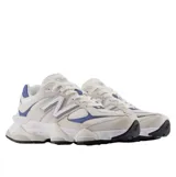 Championes New Balance modelo 9060, con diseño futurista inspirado en la estética Y2K. Presentan una combinación de tonos beige y blanco con detalles en azul vibrante. Cuentan con una entresuela esculpida de proporciones exageradas que incorpora tecnologías de amortiguación ABZORB y SBS para mayor confort y estabilidad.