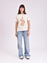 Remera de manga corta color beige claro con cuello redondo y un estampado central de una serpiente estilizada en tonos naranja y turquesa.