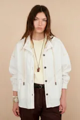Chaqueta blanca de lino con cuello camisero, cierre con botones a tono, mangas largas con puños abotonados, bolsillos laterales y costuras a contraste.