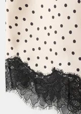 Top de poliéster color crudo con estampado de lunares negros, diseño asimétrico con detalles de puntilla negra en el escote y el ruedo.