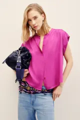 Camisa sin mangas de corte amplio y color fucsia, con cuello mao y cierre frontal de botones ocultos.
