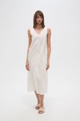 Vestido midi de algodón color crudo, con cuello en V, sin mangas y diseño holgado. Presenta un delicado bordado lineal en forma de zigzag que recorre toda la prenda.
