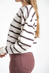 Sweater de algodón con diseño de rayas horizontales en color marrón sobre fondo crudo. Presenta un corte oversize, cuello redondo y puños acanalados, con un pequeño detalle bordado en la parte inferior.