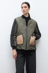 Campera bomber reversible con diseño capitoneado, cuerpo en color verde oliva y mangas negras. Presenta cierre frontal, cuello, puños y ruedo acanalados, y un bolsillo de parche en color beige.