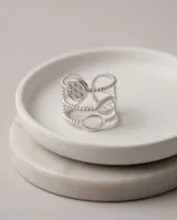 Anillo triple ajustable de acero quirúrgico plateado con detalles de circonias, compuesto por tres bandas: una con un dije circular pavé, otra con aros ovalados y otra con textura de esferas.