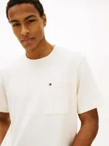 Remera Tommy Hilfiger de corte amplio y estilo urbano, confeccionada en punto de malla de mezcla de algodón en color blanco. Presenta cuello redondo, hombros ligeramente caídos y un bolsillo de parche en el pecho con el logo bordado.