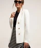 Blazer alargado de punto roma color blanco, con cuello solapa, bolsillos frontales y botones dorados.