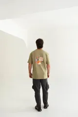 Remera color arena de algodón, con cuello redondo y mangas cortas. Presenta un estampado pequeño en el frente de una porción de pizza con contorno azul.