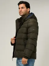 Campera puffer Tommy Hilfiger de color verde militar, con diseño acolchado horizontal, capucha integrada con interior azul y cierre frontal de cremallera. Cuenta con bolsillos laterales con cierre y el logo bordado en el pecho.