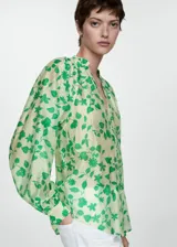 Blusa de tejido semitransparente con estampado floral en tonos verdes sobre fondo claro. Presenta escote en pico, cierre frontal con botones y mangas largas abullonadas con puños abotonados.