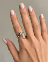 Anillo ajustable de acero color plateado, con diseño abierto y detalle de gota voluminosa en un extremo.