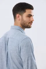 Camisa de manga larga confeccionada en mezcla de lino y algodón, con sutiles rayas celestes, cuello camisero clásico y cierre frontal de botones.
