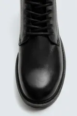 Bota tipo derby de cuero negro con cordones al tono, horma redonda y suela track con ligero tacón.