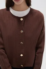 Cardigan de tejido acrílico con textura acanalada, corte ajustado al cuerpo, cuello redondo y cierre frontal con botones metálicos.