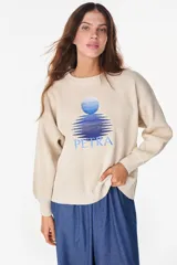 Sweater de punto color beige con cuello redondo, mangas largas abullonadas y puños y ruedo acanalados. Cuenta con un diseño bordado en el pecho que representa un sol sobre el agua y la inscripción 'PETRA'.
