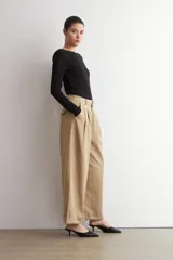 Pantalón pinzado beige de corte ancho y relajado, tiro alto, con bolsillos laterales y detalle de doblez en los bajos.