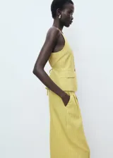 Pantalón de tiro alto color amarillo con sutil diseño de rayas verticales, de corte recto y largo, con bolsillos laterales y cierre frontal de botón y cremallera.